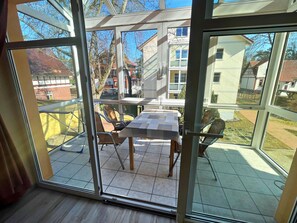 A glass-enclosed balcony with a table and chairs, a view of the neighborhood, and a clear sky.
