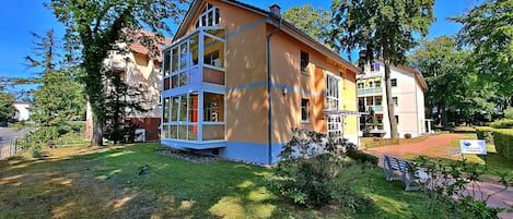 Un bâtiment à deux étages doté d’un balcon, entouré de verdure et d’arbres.