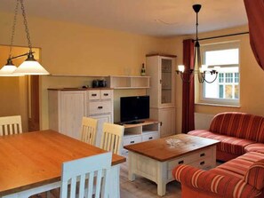 En kompakt opholdsstue med spisebord, stole, sofa, fjernsyn og skabe.