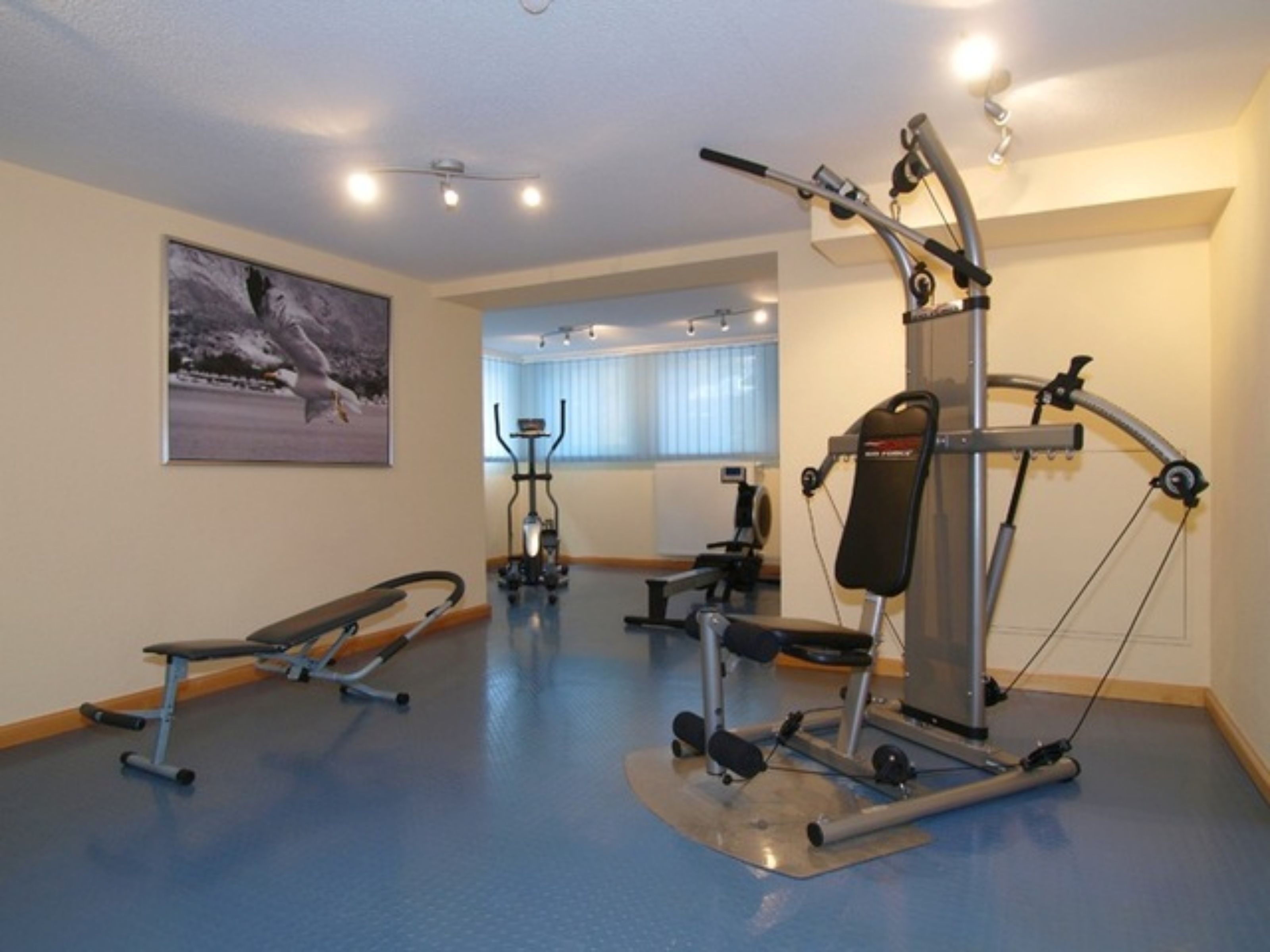 Une salle de sport équipée de matériel d’exercice, d’un banc et d’un tableau accroché au mur.