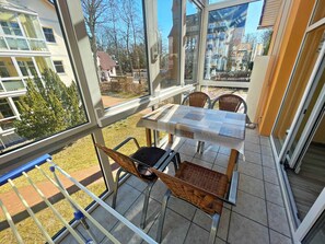En balkon med et bord og stole, udsigt over kvarteret og et gelænder.