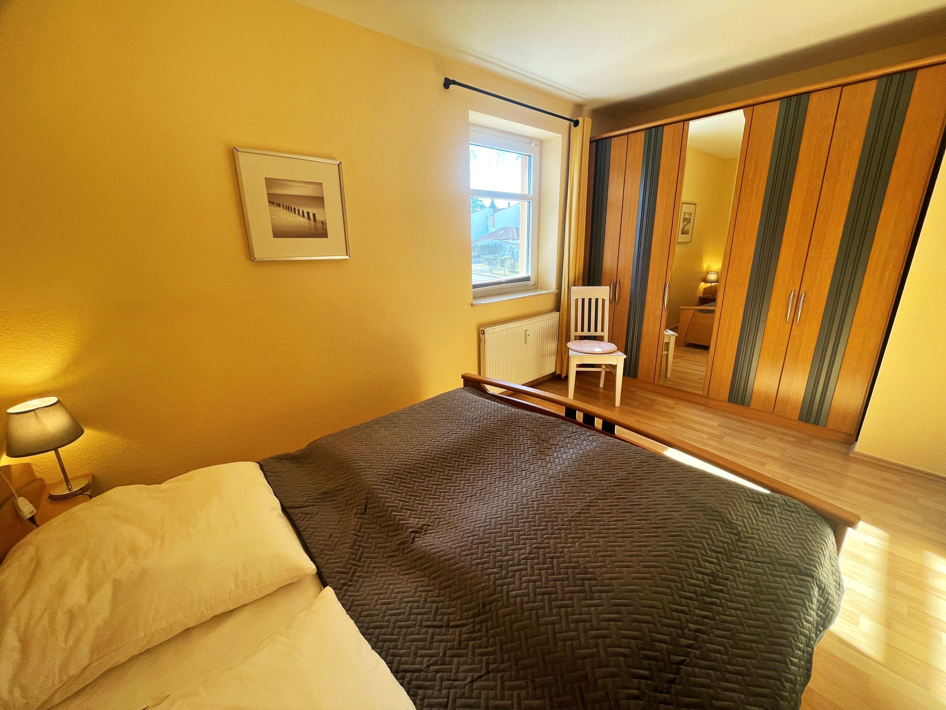 A bedroom with a bed, a chair, a window, and a wardrobe.