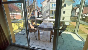 Un balcón acristalado con una mesa y sillas, vista al vecindario y cielo despejado.