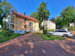 A yellow building with a red roof, a white car parked in front, and a paved walkway. - Ostseepark Waterfront Galeone 44 - Galeone 44 (Heringsdorf)