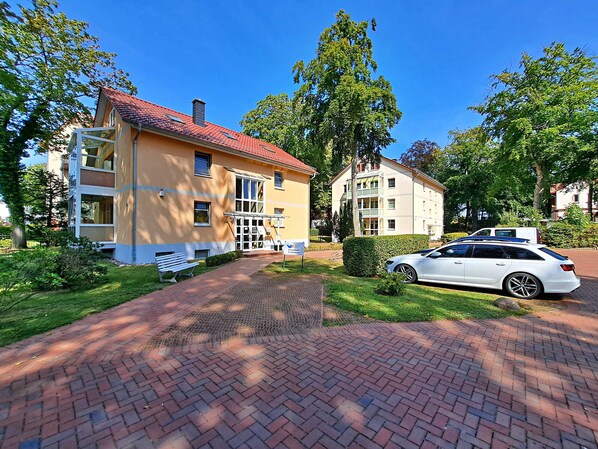 A yellow building with a red roof, a white car parked in front, and a paved walkway.