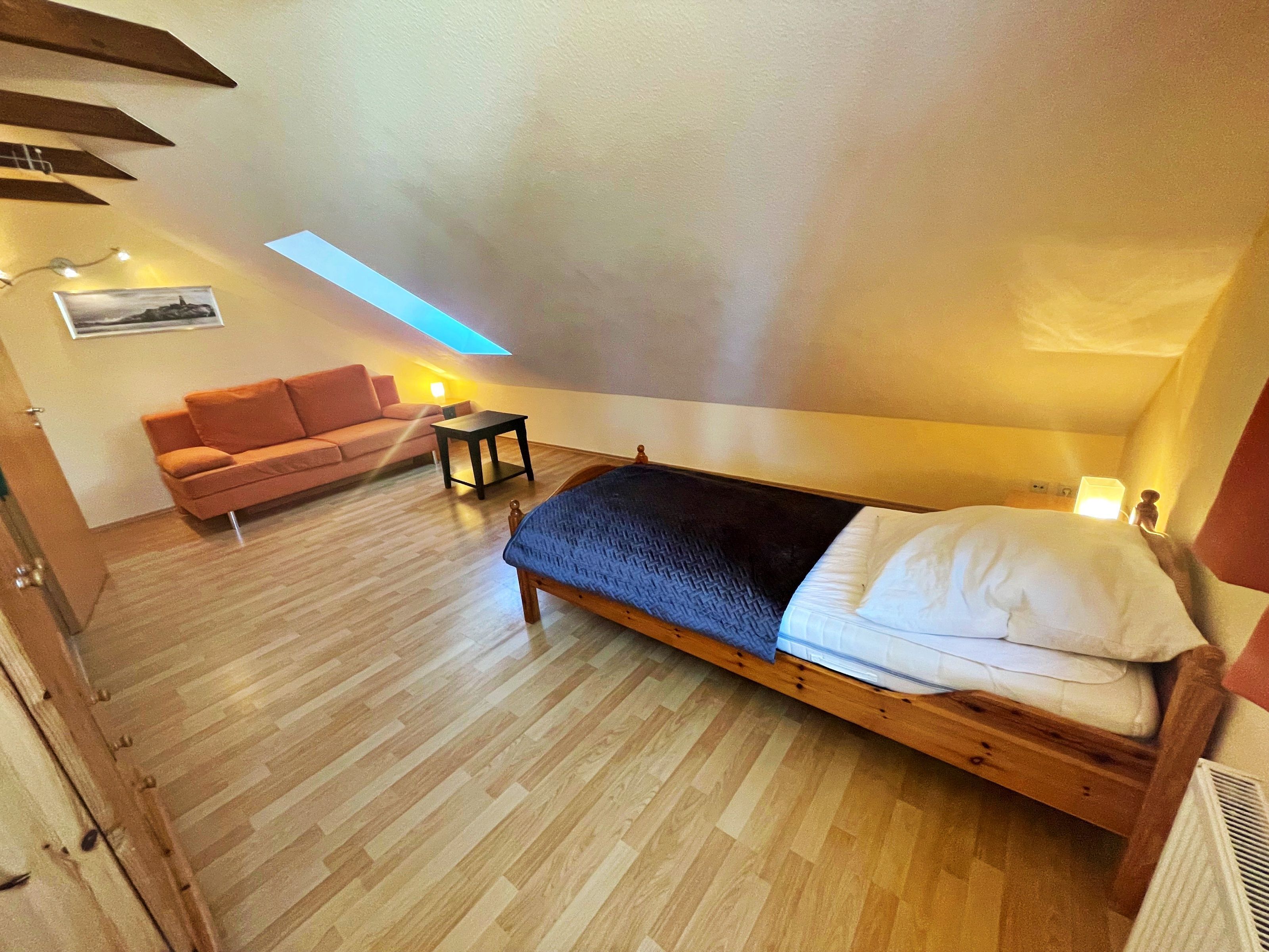 Una camera da letto con un letto di legno, un divano, un tavolino e un lucernario.