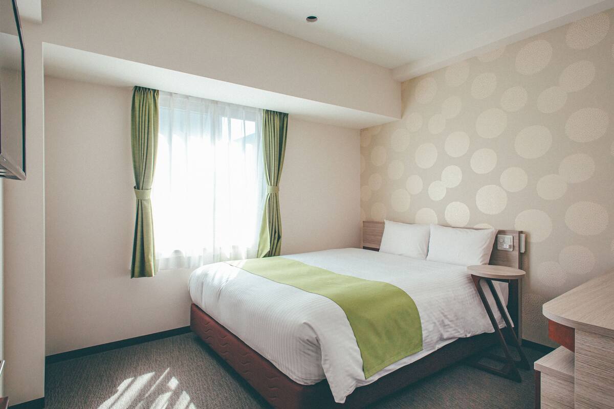 A hotel room with a large bed, a bedside table, a nightstand, and a window with curtains.