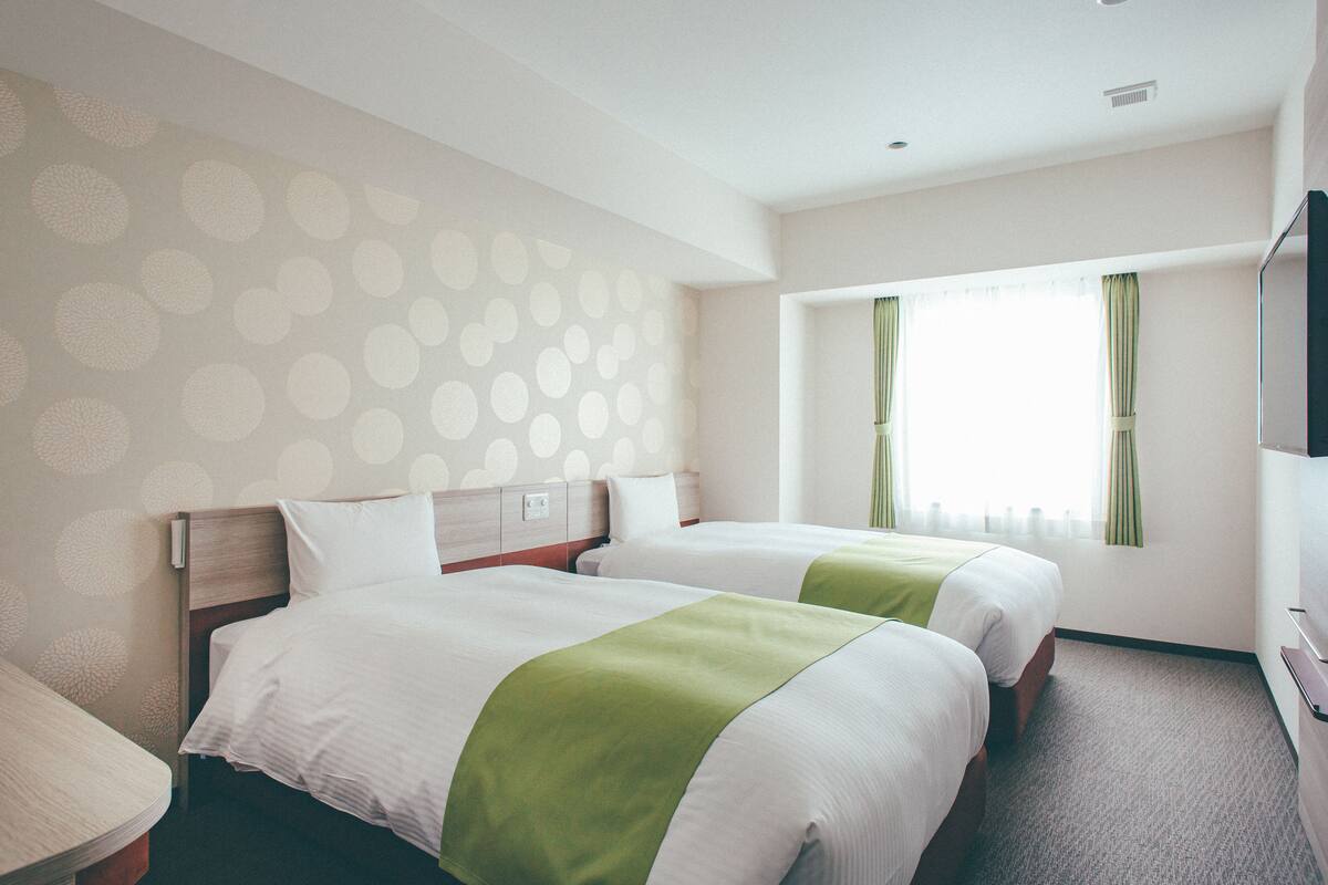 A hotel room with two beds, a TV, and a window with curtains.
