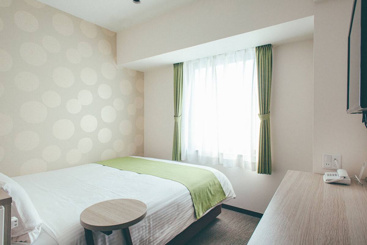 A hotel room with a bed, a bedside table, a telephone, and a window with curtains.