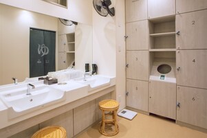 A bathroom with three sinks, a mirror, a fan, and wooden lockers numbered 1 to 6.