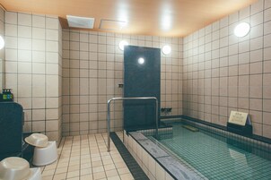 Un bagno pubblico con pavimento piastrellato, un lavandino nero e zona doccia con pareti in vetro.