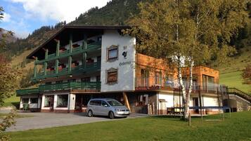 Traditional alpine-style hotel with a white facade and green balconies, offering a serene hillside setting.