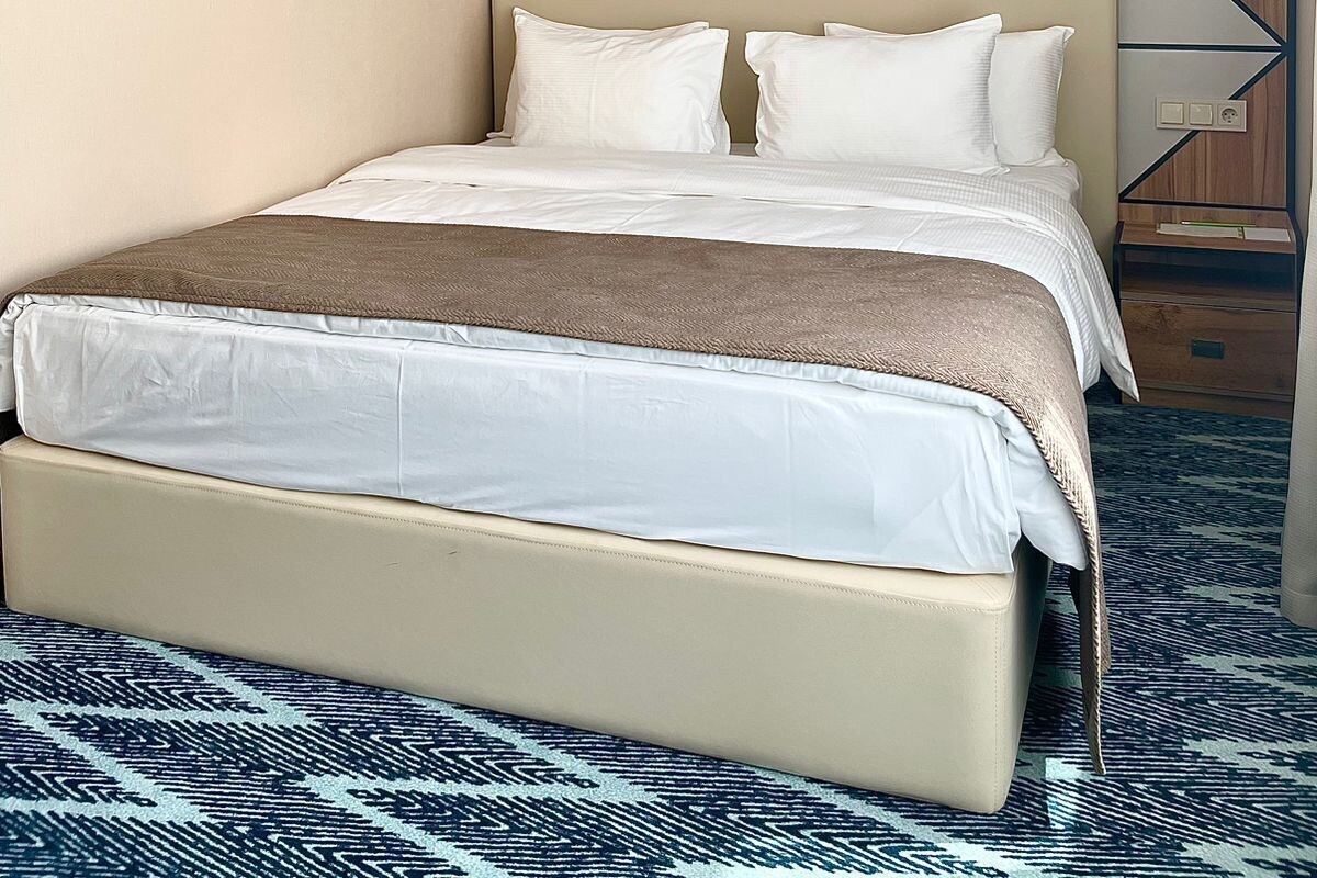 Una habitación de hotel con una cama, cabecera con motivos geométricos, una obra de arte en la pared y una alfombra estampada.