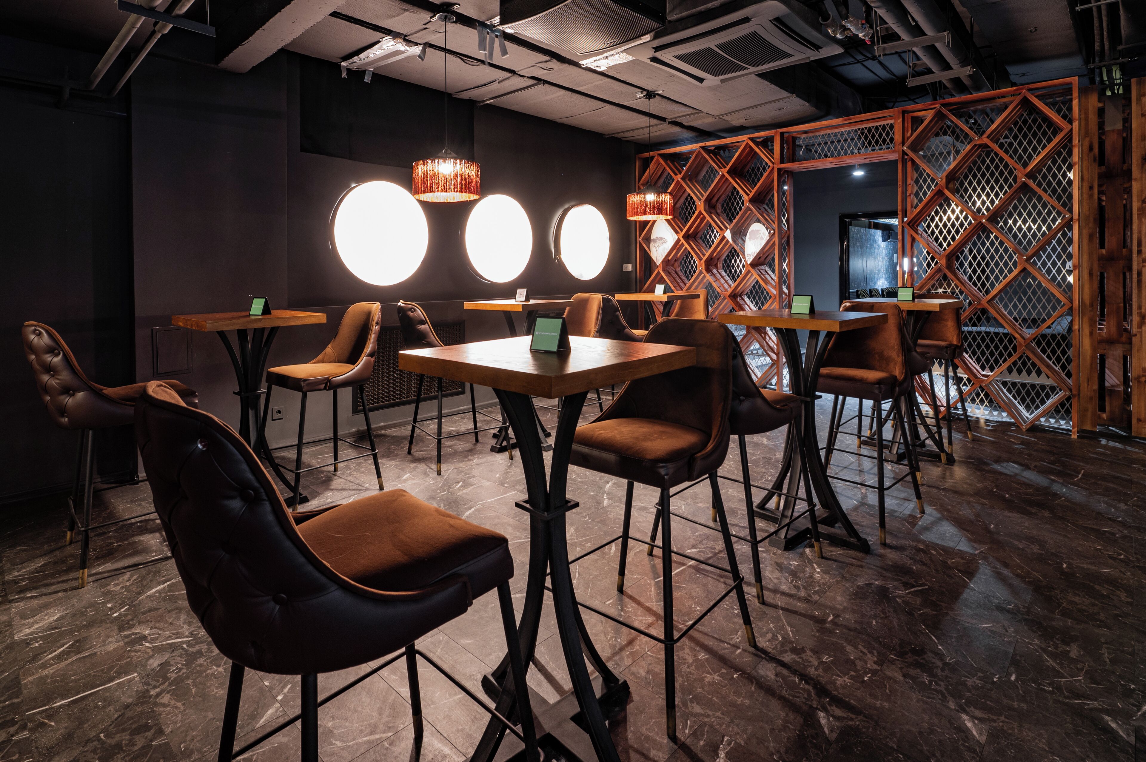 Un interior moderno con mesas redondas y sillones de cuero, separadores de madera e iluminación colgante.