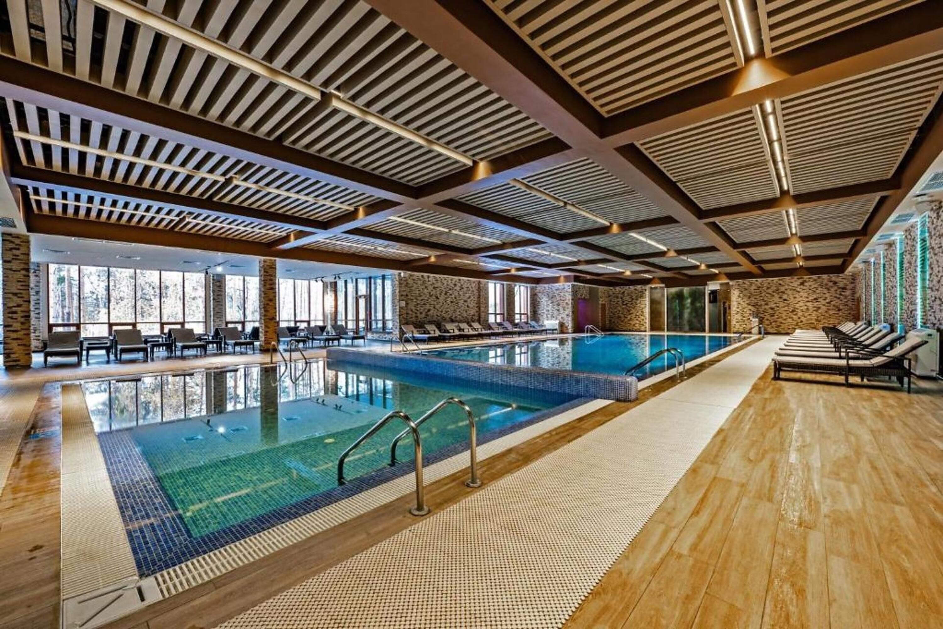 A large indoor swimming pool with multiple lanes, lounge areas with chairs, and a stone wall.