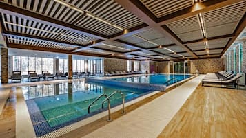 A large indoor swimming pool with multiple lanes, lounge areas with chairs, and a stone wall.