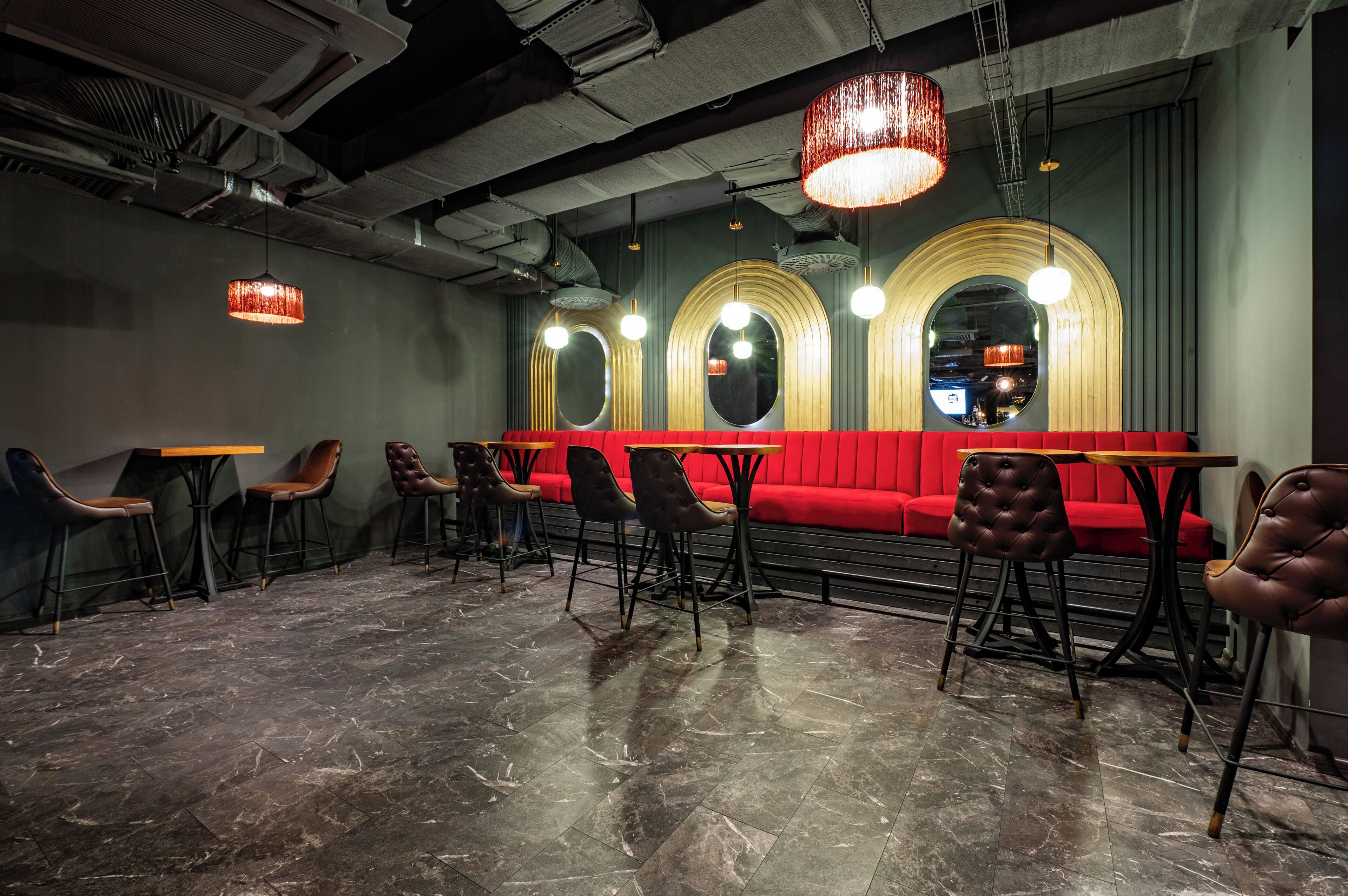 A restaurant with a red booth seating area, black chairs, and a marble floor.