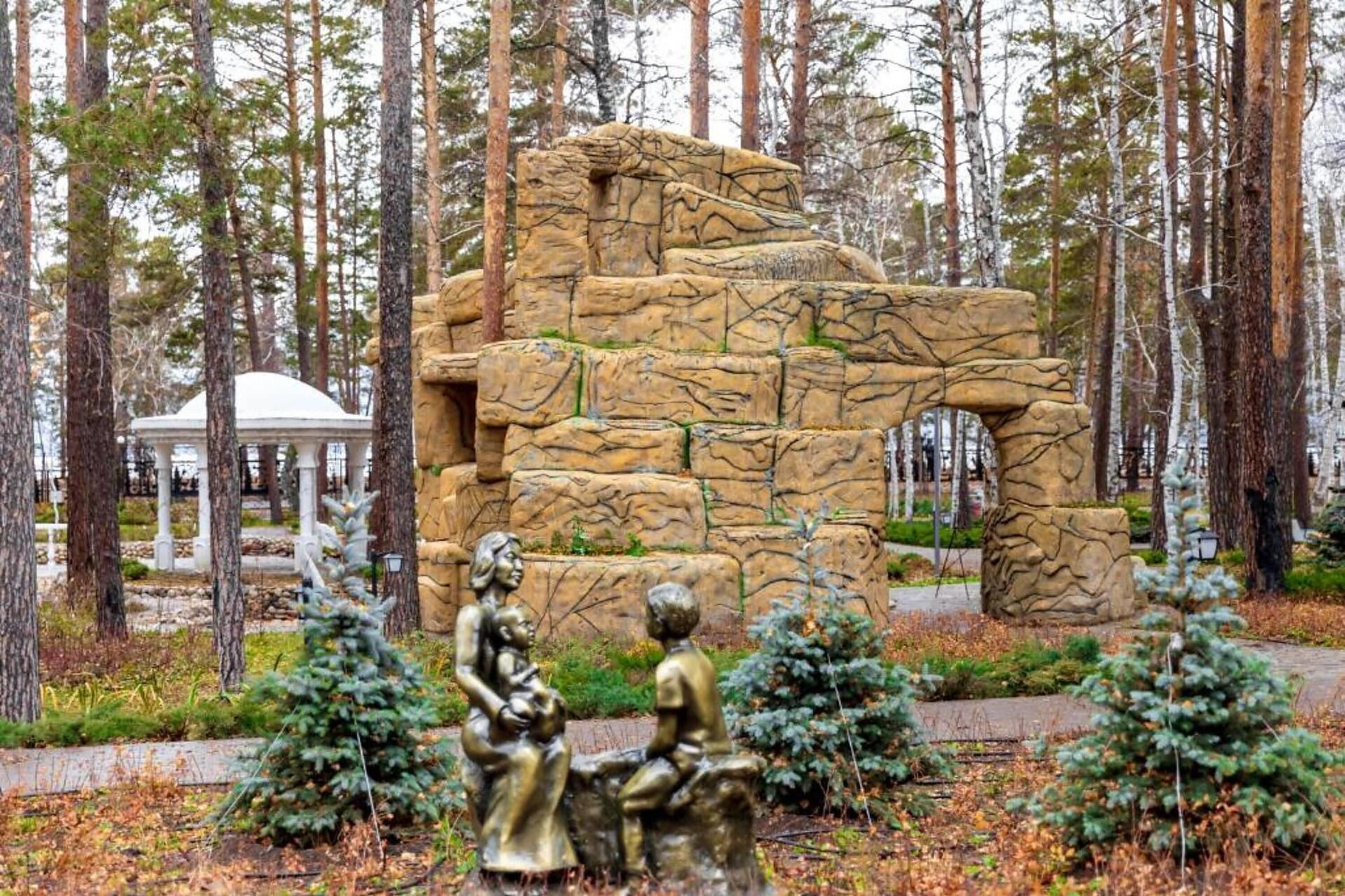 A park with a large rock sculpture, a gazebo, and two bronze statues.
