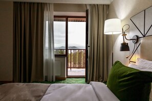 Habitación de hotel con una cama, un almohadón verde, una lámpara fijada a la pared y vistas a un balcón con barandilla.