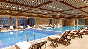 A large indoor swimming pool with multiple lounge chairs and a stone wall backdrop.
