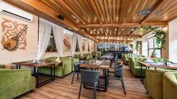 Un restaurante con vigas de madera en el techo, asientos tapizados en verde y una barra de fondo.