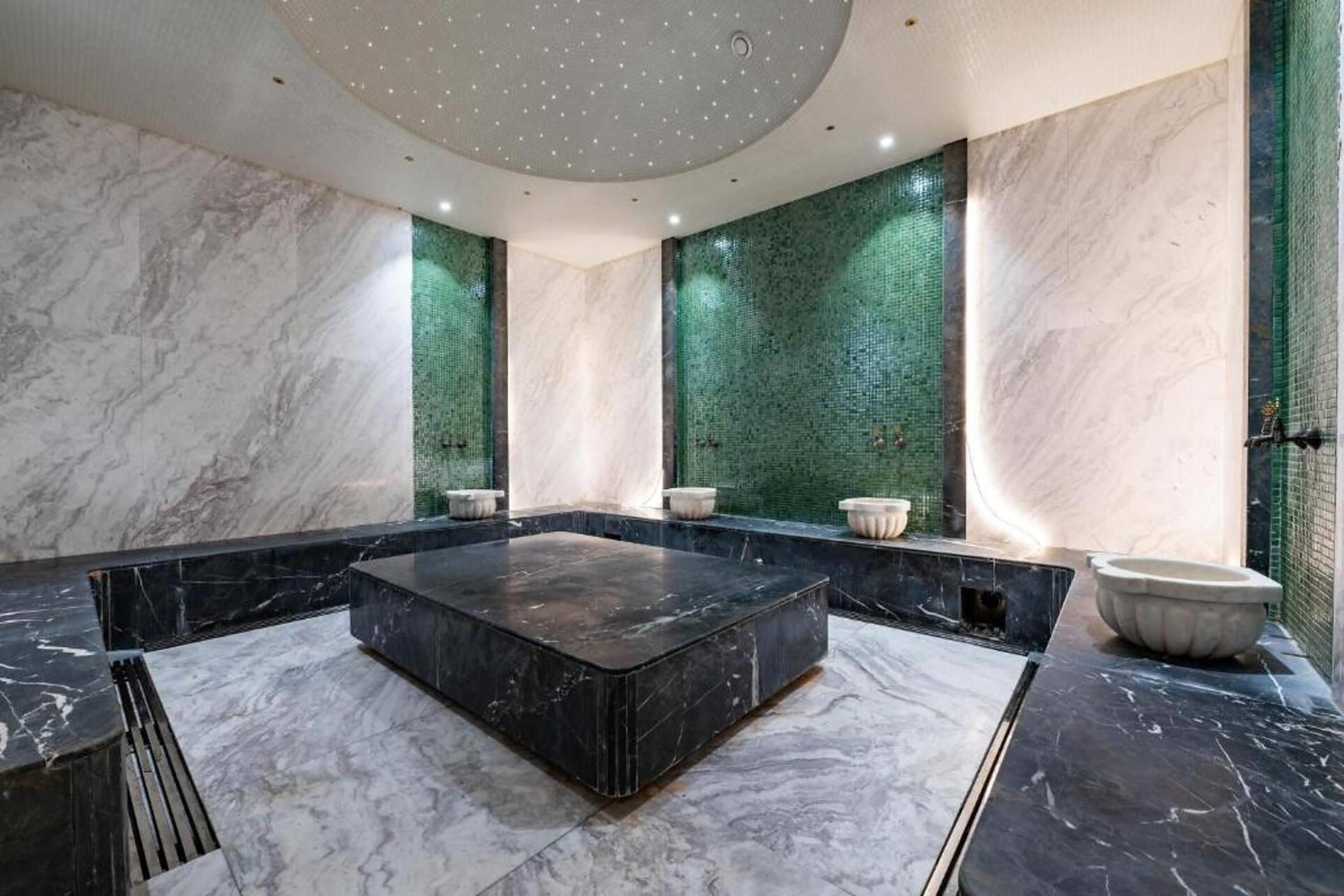 Une salle de bain moderne avec une baignoire centrale en marbre noir, des murs en marbre blanc et des panneaux de mosaïque verte.
