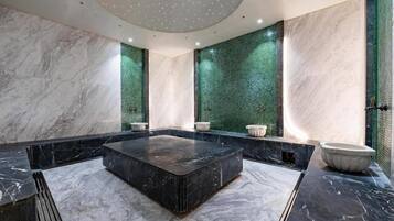 Une salle de bain moderne avec une baignoire centrale en marbre noir, des murs en marbre blanc et des panneaux de mosaïque verte.