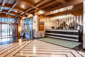 Un hall d’hôtel avec un comptoir d’accueil, une grande fenêtre et une moquette verte ornée du nom de l’hôtel.