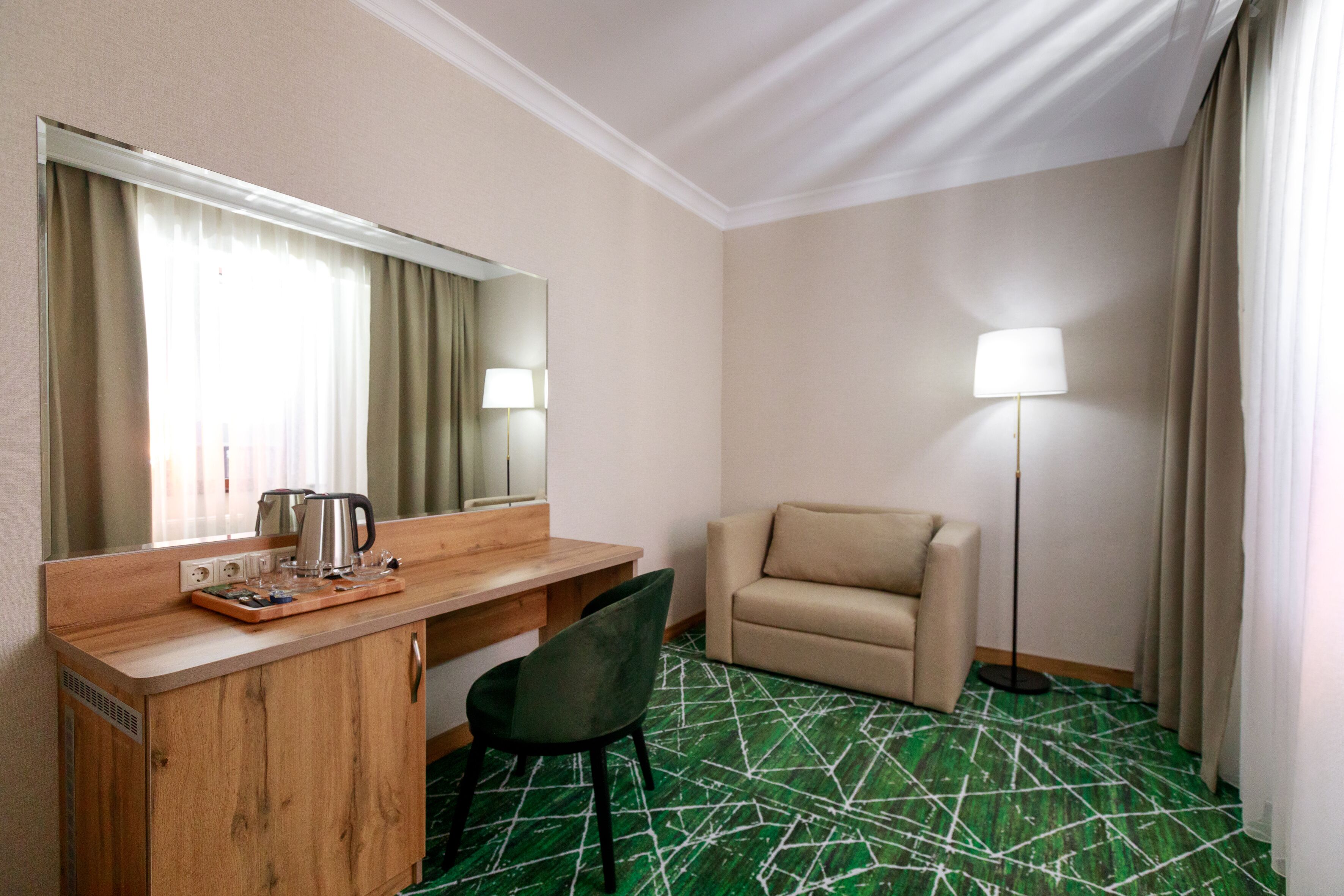 Ett hotellrum med ett skrivbord i trä, en stol, en soffa, en golvlampa och en stor spegel.