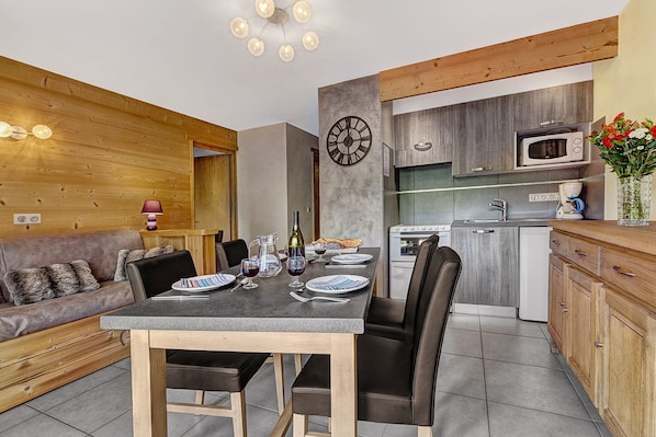 A compact kitchen with a dining area, wooden accents, and a modern clock.