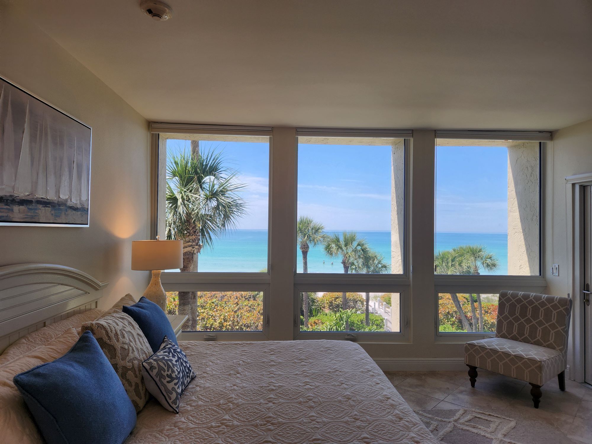 Quarto com uma cama grande, uma cadeira e vista para o oceano através de janelas amplas.