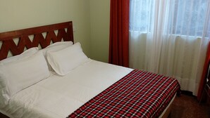 A bed with a wooden headboard, white bedding, and a red plaid bedspread. - Sumawe Suites Karatu (Karatu)