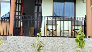 A two-story house with a sloped metal roof, a balcony with a metal railing, and a stone wall in front. - Sumawe Suites Karatu (Karatu)