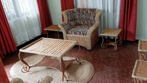A room with a wicker armchair, a small table, a round table, and a matching stool. - Sumawe Suites Karatu (Karatu)