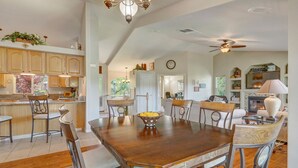 Une cuisine spacieuse avec des meubles en bois, un coin repas doté d’une grande table et de chaises en bois, et un salon avec une cheminée et des fauteuils.