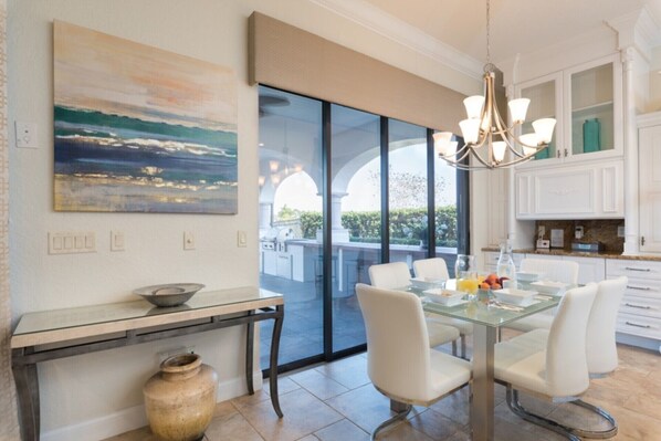 Comedor moderno con una mesa de vidrio, sillas blancas y vistas a un patio con piscina.