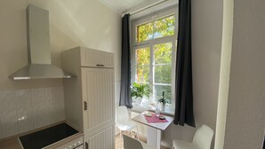 A kitchen with a stove, oven, and cabinets, a dining table with chairs, and a window with curtains. - Ferienwohnung König Georg (Wurzen)