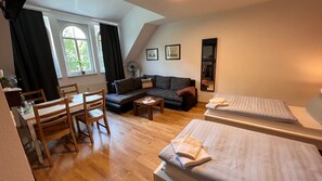 A cozy living room with a sofa, a dining table with chairs, a small coffee table, and a bed with a striped blanket. - Ferienwohnung König Georg (Wurzen)