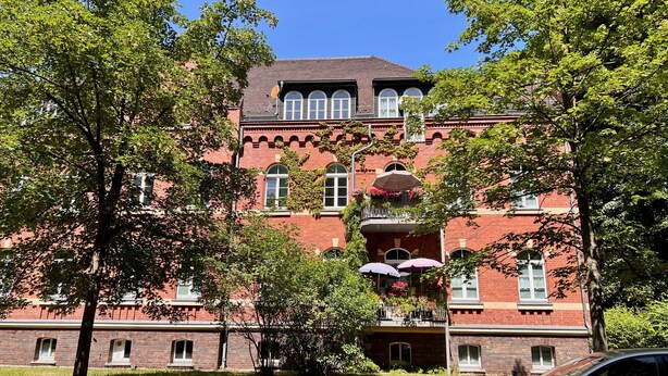 A large red brick building with multiple windows and balconies, surrounded by trees. - Ferienwohnung König Georg (Wurzen)
