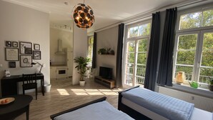A modern bedroom with two beds, a desk, a TV, and a balcony with a view of trees. - Ferienwohnung König Georg (Wurzen)