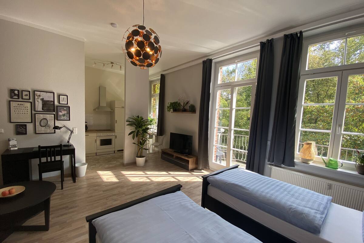Une chambre moderne avec deux lits, un bureau, une télévision et un balcon donnant sur la verdure.