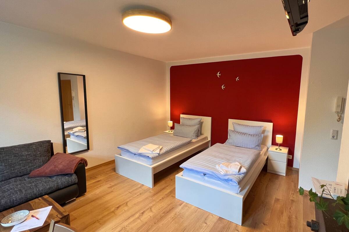 Une chambre d’hôtel de taille modeste, comprenant deux lits simples, un canapé, une petite table et un miroir.