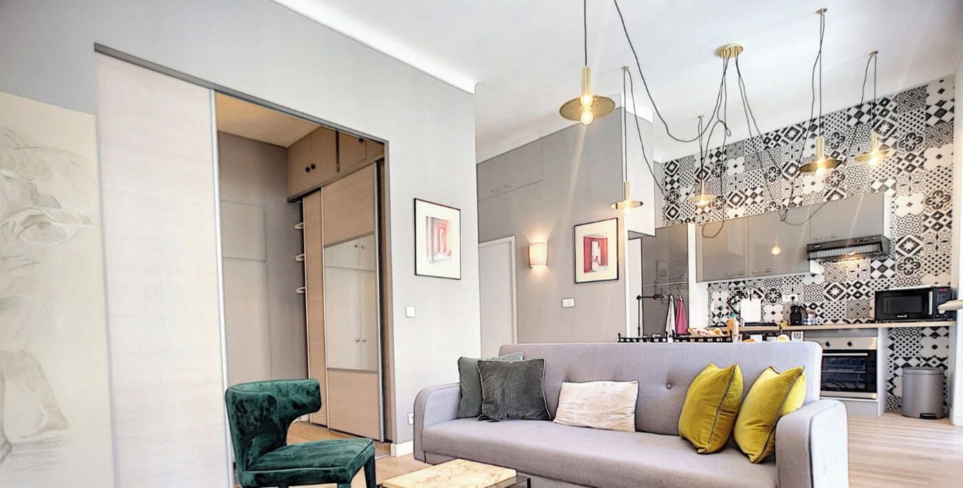 A modern living room with a sofa, a green chair, and a kitchen area with patterned tiles.