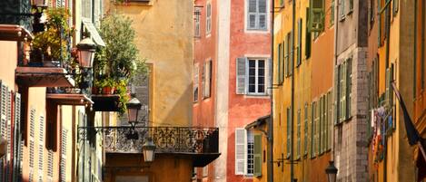 A narrow street with colorful buildings, balconies with plants, and traditional street lamps.