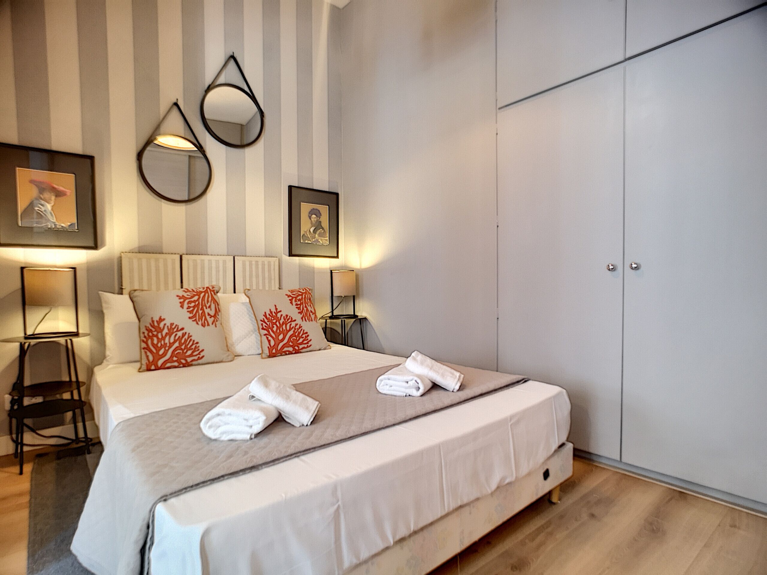 A neatly made bed with white linens and decorative pillows, a bedside table with a lamp, and a wardrobe with a handle.