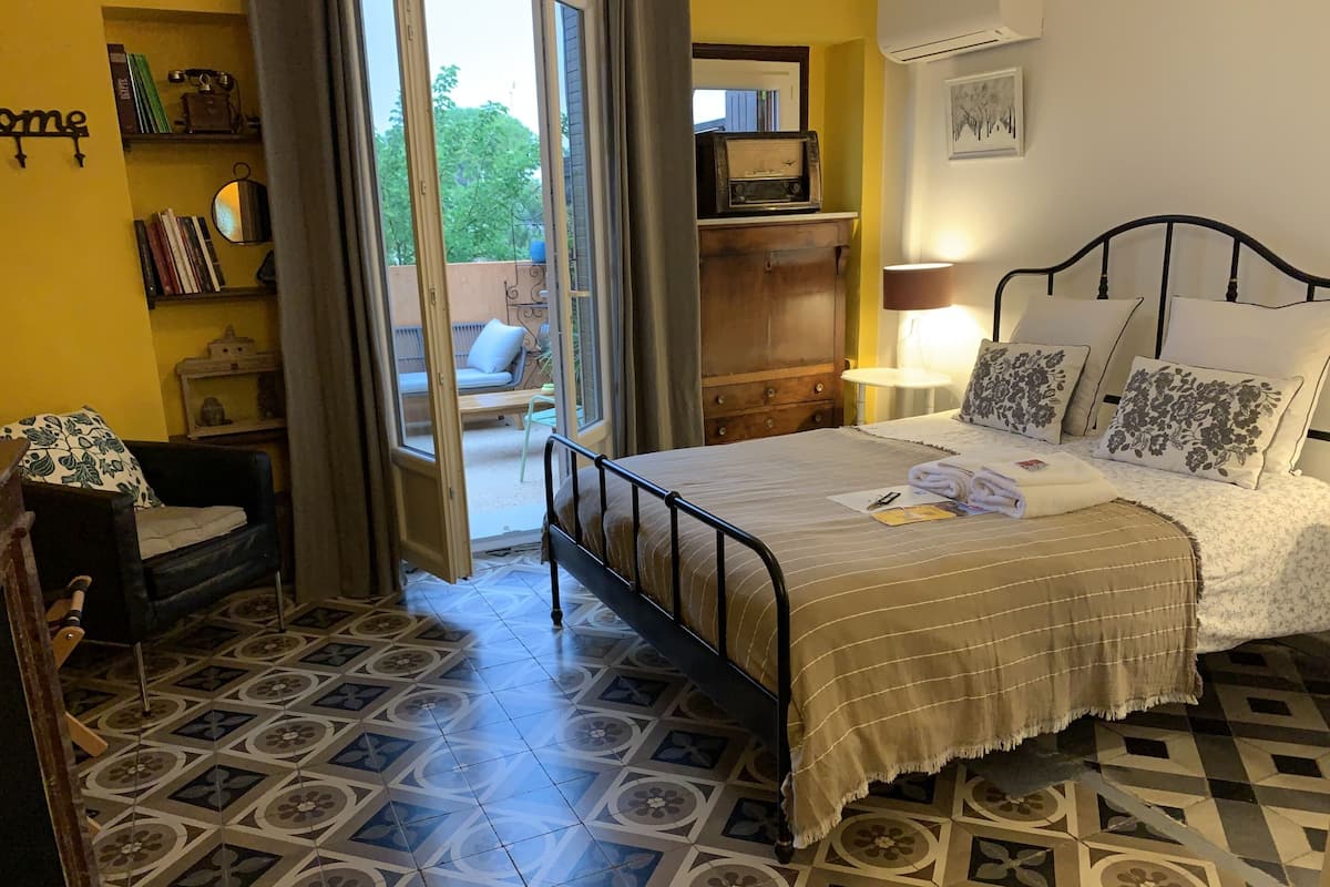 A bedroom with a bed, a chair, a desk, a bookshelf, and a window.