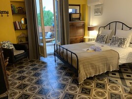 Un dormitorio con cama, una silla, un escritorio, una estantería y una ventana.
