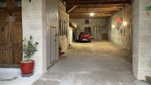 A narrow, dimly lit corridor with a red car parked at the end, flanked by stone walls and wooden doors. - Lo Componaïro (Pouzols)