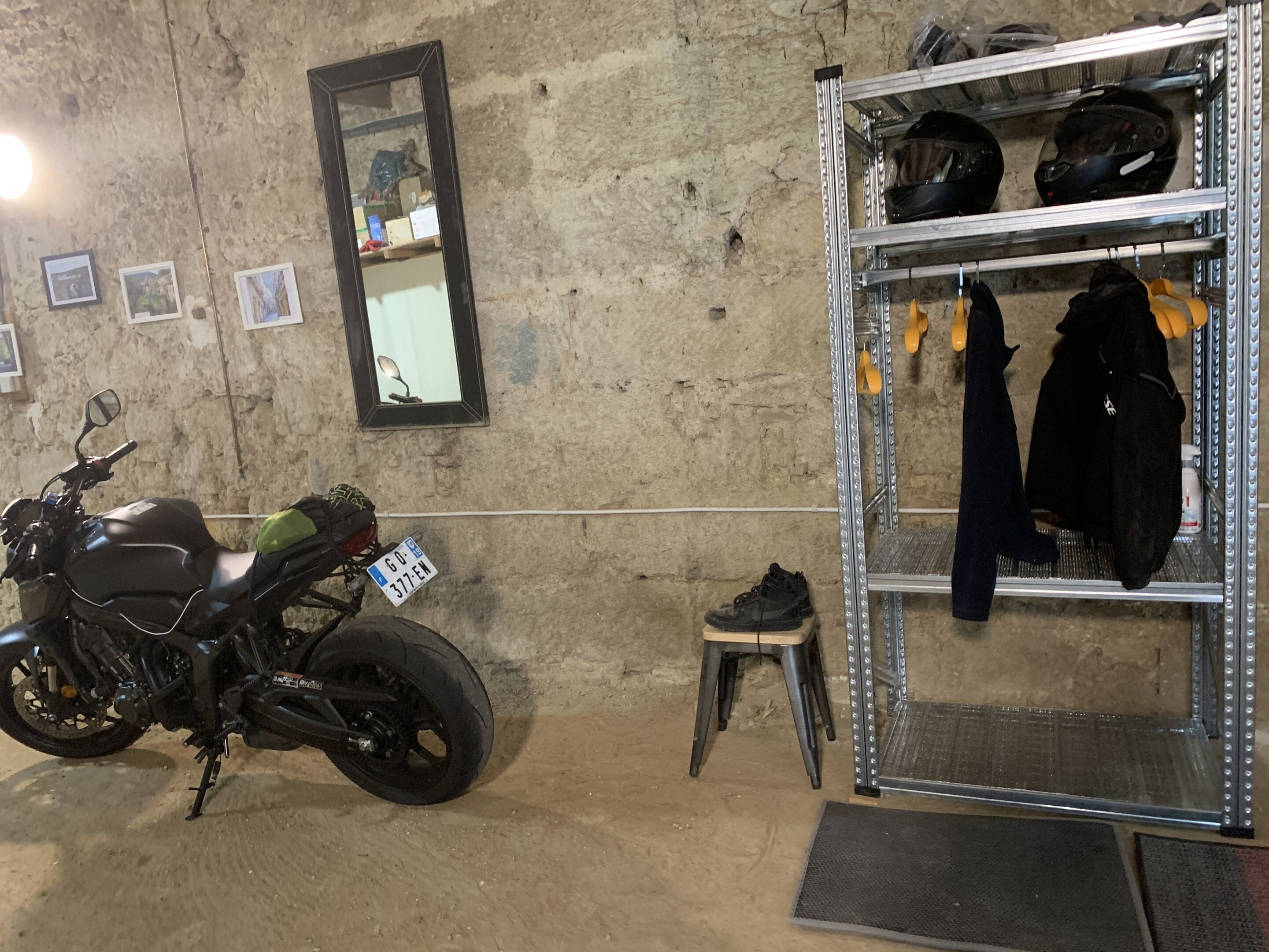 A motorcycle parked in a garage with a metal shelf containing helmets and jackets.