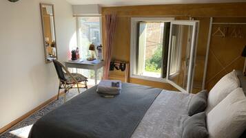 Een slaapkamer met een bed, een bureau met stoel, een raam met gordijnen en een spiegel aan de muur.